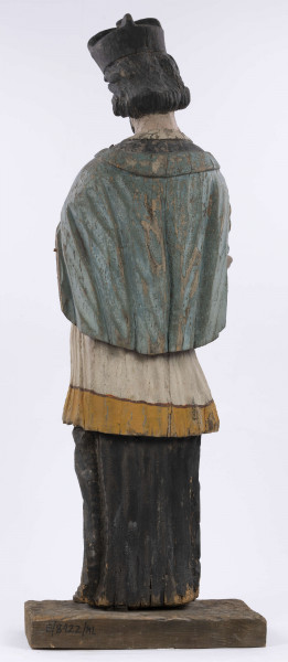 E/8422/ML - Rzeźba drewniana, pełna, polichromowana, przedstawiająca św. Jana Nepomucena. Zakomponowana frontalnie, z rękoma zgiętymi w łokciu i lekko rozłożonymi. Twarz owalna, pomalowana białą farbą. Małą broda i krótkie czarne wąsy. Nos krótki, prosty. Oczy owalne podkreślone czarnym konturem. Brwi łukowate, wąskie, czarne. Włosy czarne, ułożone w pukle. Na głowie czarny biret. Długa czarna sutanna, biała komża ozdobiona u dołu złotą koronką. Na piersiach krzyż, zawieszony na łańcuchu. Na komżę narzucona jasnoniebieska peleryna. Stopy lekko rozstawione. Obuty w sandały o jednym pasku. 

Konserwacja: 1990 r.