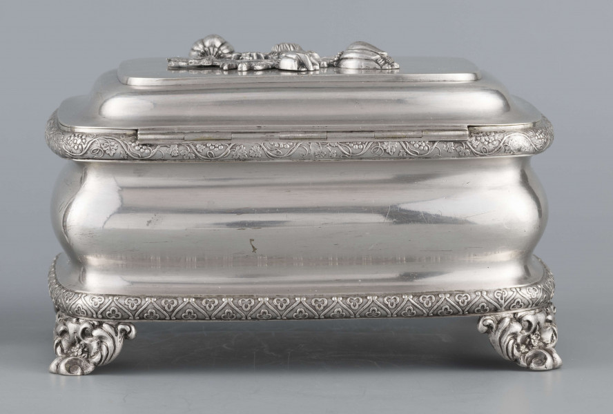 S/Mt/469/ML - Cukiernica prostokątna o zaokrągłonych narożach, profilowana, na czterech akantowych nóżkach. Brzeg dolny i górny obwiedzione półwałkiem zmoletowanej taśmy: u góry z wzorem winorośli, na dole - trójliścia.Brzeg wieczka fasetowany, z przodu lekko wywinięty tworzy uchwyt. Na wieczku nałożona półplastyczna plakieta w postaci  asymetrycznej gałązki kwiatowej. Szyld zamka stanowi sztancowana plakieta z motywem winorośli. Wnętrze złocone.
Na dnie sygnatura wypukła we wklęsłych ramkach:
- J.Suchocki
- w Lublinie
i punca z oznaczeniem próby 