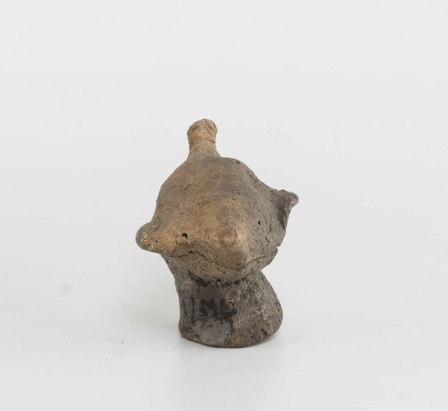Figurka zoomorficzna w kształcie ptaszka, wykonana schematycznie. Nóżka walcowata. Główka, ogon oraz skrzydełka ledwie zaznaczone. Powierzchnia gładzona niestarannie. Sklejone, uzupełnione gipsem. Surowiec - glina z domieszką drobnoziarnistą. Barwa Szarobrunatna. Wypał dobry.
Wymiary dodatkowe: 1,3 cm (śr. stopki), 2,4 cm (rozstaw skrzydełek)