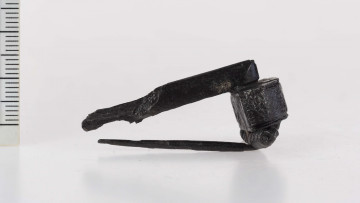 640/A/ML/4 - Fibula żelazna zachowana częściowo, pierwotnie kształu prawie prostokątnego. Grzebień zdobiony przy krawędziach linią i karbowaniem przy krawędziach bocznych. Kabłąk prosty, pochewka ukruszona. 