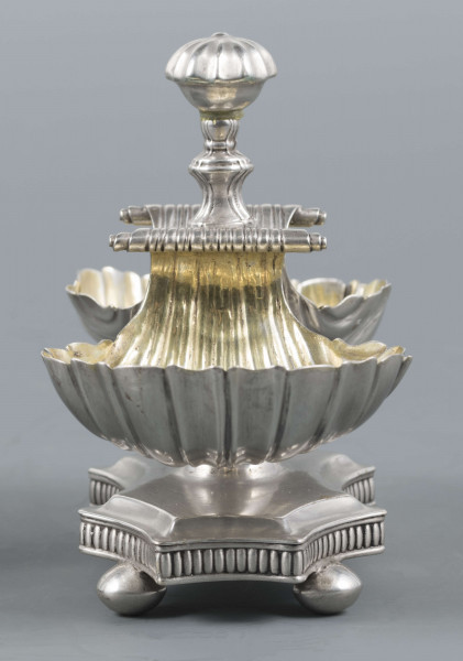 S/Mt/494/ML - Solniczka składa się z dwóch czarek w formie muszli połączonych z pionowym, profilowanym uchwytem o zwieńczniu w formie makówki ustawionym na wydłużonej ośmiobocznej podstawie o wklęsłych bokach. Krawędź podstawy fasetowana, boki karbowane, cztery nóżki w kształcie spłaszczonych kulek. Wnetrze muszli złocone.
Na dnie podstawy sygnatura kursywą w owalnych ramkach:
- J.Gałecki
- w Lublinie
- punca owalna z przedstawieniem dłoni (sygnatura pomocnicza)
- wężyk probierczy
- znak probierni warszawskiej z próbą 