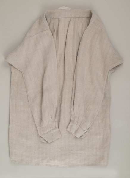 E/9858/ML - Koszula męska z lnianego samodziałowego płótna tkanego splotem prostym, szyta na maszynie. Krój z karczkiem. Wycięcie koło szyi wykończone stójką z białego płótna zapinana na jeden guziczek. Rozcięcie na przodzie o dł. 26 cm zapinane na dwa guziczki, wykończone fałdem o szer. 4,5 cm. Gors naszyty jest cienkim białym płótnem. Rękawy długie, krojone, razem z włokami dołem wzbogacone ośmioma zakładkami ujęte w mankiet o dł. 24 cm szer. 4 cm zapinany na guziczek.