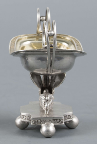 S/Mt/359/ML - Solniczka w kształcie prostokątnej łódki z dwoma wolutowymi uchami z okrągłego drutu, umieszczonej na figurce gryfa, z  podstawą prostokątną o wklęsłych narożach i czterech nóżkach w formie spłaszczonych kulek. Brzeg łódki wywinięty, wnętrze złocone. Brzegi łódki i boki podstawy obiega moletowana taśma z ornamentem roślinnym.