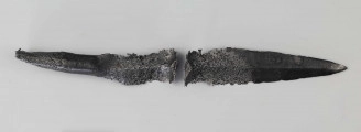 Żelazny grot oszczepu z ostrym żeberkiem środkowym, zgięty rytualnie (złamany w miejscu zgięcia). Grot stanowi element wyposażenia ciałopalnego pochówku złożonego prawdopodobnie w popielnicy. Odkrycia dokonano w 1959 roku przypadkowo w czasie prac rolnych. Oprócz trzech grotów, pochówkowi wojownika towarzyszyły: żelazne umbo, dwie ostrogi, tok brązowy (prawdopodobnie okucie drzewca oszczepu) a także żelazny miecz z miedziana inkrustacją wyobrażającą rzymskich bogów. Pochowany na terenie obecnej wsi Podlodów wojownik należał do elity wojskowej przedstawicieli kultury przeworskiej.
