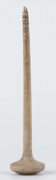 E/8019/ML - Przęślica krężołkowa z drewna brzozowego składa się z cienkiej deski – przysiadki, w której przy jednym końcu osadzona jest pionowa beleczka zw. piórem, z nasadzonym od góry ruchomym krężlem w kształcie wydłużonego stożka. Deseczka przysiadki o kształcie prostokątnym lekko zwężającym, od ok. połowy swej długości w kierunku pióra, i zakończonym głową zwierzęcą – psa. Pióro i krężel ozdobnie toczone. Krężel ma kształt stożka z rozszerzoną podstawą, w której znajduje się stożkowaty otwór, do osadzenia krężla na piórze. Dekoracja snycerska ryta znajduje się na zwężającej części przysiadki. Część zdobiona oddzielona małym stopniem. Grubość przysiadki w części zdobionej 2x większa od pozostałej części. Dekoracja snycerska tworzy ornament roślinny w postaci trzech ulistnionych drobno gałązek. Na zakończeniu ornamentu znajdują się ryte liście oraz inicjały „K.F.”. Głowa psa zdobiona drobnymi nacięcia. Zakończenie przysiadki wycięte faliście.