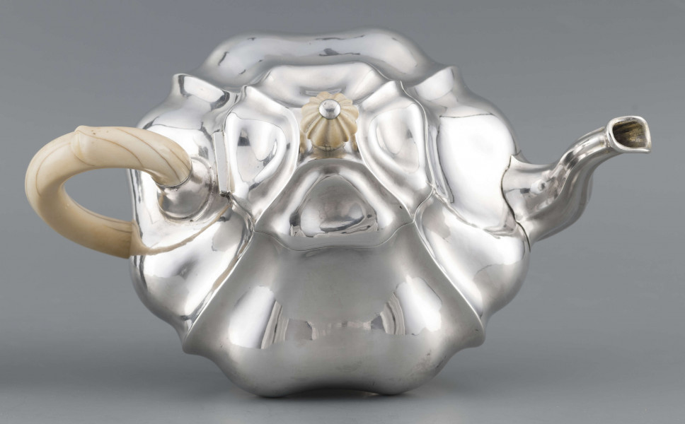 S/Mt/500/ML - Korpus silnie wybrzuszony w części środkowej, puklowany pionowo, profile przechodzą na pokrywke w formie wieczka na zawiasie. Stopa kwadratowa wielolistna, wylew w formie dzióbka, ucho kościane osadzone w dwóch tulejkach,
uchwyt na pokrywce kościany, profilowany. Wnetrze złocone.
Na spodzie stopy sygnatura:
- 