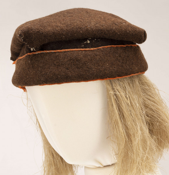 Czapka męska rogatywka szyta ręcznie z samodziałowego sukna w kolorze brązowym. Jeden pas stanowi otok., drugi tej samej szerokości jest wywinięty na wierzch i obszyty na dolnej i górnej krawędzi pomarańczowym wełnianym sznureczkiem. Górna cześć czapki wykonana z kwadratowego płata z wywiniętymi narożnikami, które po zszyciu i przyszyciu do otoka tworzą płaskie kwadratowe denko, o wym. 20 x 20 cm. Noszona do sukmany.