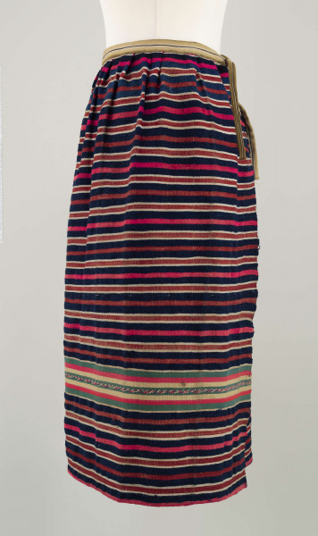 E/7351/ML - Zapaska wełniana w granatowe, czerwone, białe i amarantowe paski biegnące w poprzek. Zszyta z dwóch części – pionowy szew na przodzie. Dołem ozdobiona szerokim szlakiem dekoracyjnym, złożonym z pasków: zielonych, żółtych i amarantowych. W pasie marszczona i ujęta w oszewkę z innego materiału.