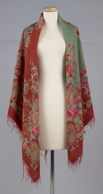 E/7995/ML - Chusta z cienkiej wełny. Powierzchnia podzielona bukietami kwiatów (róże i niezapominajki) na 4 pola w kolorach: czerwonym, zielonym, fioletowym i szafirowym. W każdym narożniku duży bukiet kwiatów oraz tzw. turecki motyw w formie łezki. Bordiura w kolorze czerwonym, na niej wieniec z większych i mniejszych bukietów. Noszona na ramionach. 