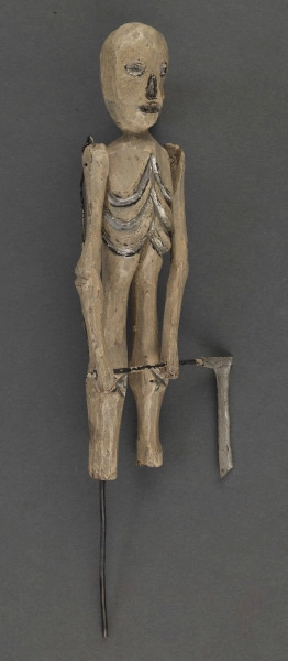 E/319/ML - Figurka z szopki, przedstawiająca śmierć, wykonana z drzewa, pomalowana białą farbą. Głowa o kształcie trójkątnym, wydłużonym. Oczy, nos i usta wydrążone i pomalowane srebrną farbą. Tułów krótki z zaznaczonymi plastycznie i zaznaczonymi srebrną i czarną farbą. Ręce ruchome w ramieniu, osadzone na drucie, w łokciu nieco zgięte z zaznaczonym plastycznie stawem łokciowym. Nogi proste, bez stóp, z silnie zgrubiałymi kolanami, z wyrzeźbionymi gwiazdkami pomalowanymi srebrną farbą. W rękach figurka trzyma kosę z drutu i cienkiej blaszki. Do ramienia przymocowany jest drut przechodzący z tyłu i założony za klamerkę wmontowaną w prawą nogę z tyłu. Drucik ten umożliwia poruszanie rękami figurki w czasie przedstawienia. W prawej nodze umocowany jest drut o haczykowatym zakończeniu.