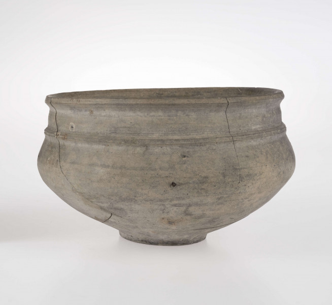 Naczynie o wklęsłym dnie, z dołkiem w centralnej części. Dno wyodrębnione niewysoką stopką. Brzusiec łagodnie profilowany. Szyjka podkreślona plstyczną listwą, w części środkowej nieco wypukła. Krawędź wylewu delikatnie wywinięta na zewnątrz. 