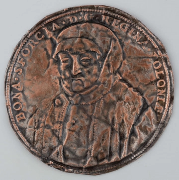 N/1495/ML - Popiersie królowej Bony lekko w lewo wzorowane na portrecie z warsztatu Cranacha. W otoku napis rozdzielony na dole przez wizerunek:
BONA . SFORCIA D . G . REGINA . POLONIAE
Dwie ostatnie litery napisu w formie ligatury.
Na zewnątrz pojedynczy otok perełkowy.
Na odwrocie pozostałość wosku?
Blacha pogięta.