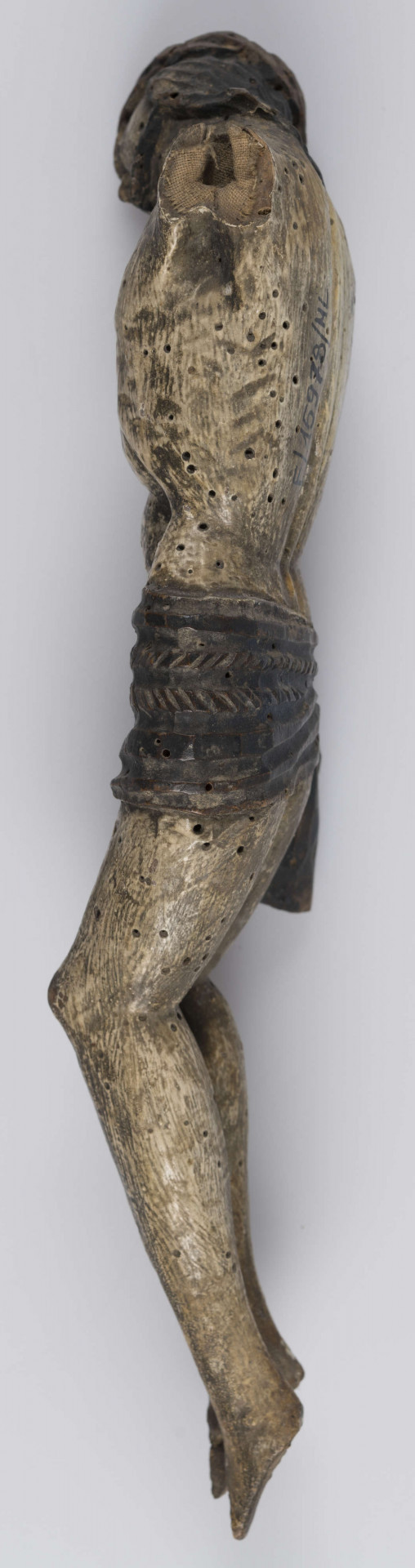 E/15978/ML - Rzeźba drewniana przedstawiająca Chrystusa Ukrzyżowanego, bez rąk. Wydłużony z wystającą klatka piersiową i linearnie zaznaczonymi żebrami, osłonięty pofałdowanym perizonium ozdobionym dekoracją snycerską w postaci ukośnych kresek. Głowa mocno przechylona , wsparta na prawym ramieniu. Twarz wydłużona o oczach osadzonych blisko siebie, nos prosty, usta wąskie okolona brodą. Na głowie korona cierniowa, włosy długie zaznaczone ukośnymi rzeźbionymi kreskami. Głowa, włosy, perizonium pokryte czarną olejną farbą, korpus biały.