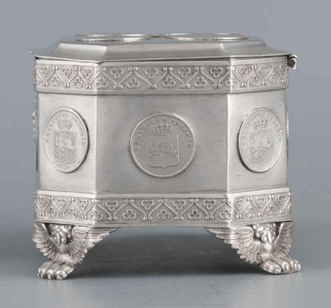 S/Mt/364/ML - Cukiernica skrzynkowa prostokątna ze ściętymi narożami, na czterech nóżkach w formie uskrzydlonych lwich łap, z wieczkiem o wklęsło profilowanym brzegu. Górny i dolny brzeg obiega  moletowana taśma z motywem neogotyckich trójliści, szyld zamka ma formę różanego wieńca pod skrzydatą główką..W ścianki i wieczko wmontowanych jest 15 monet srebrnych:
1 ort Zygmunta III
1 talar pruski, 1818 r.
1 pięciofrankówka, 1811 r.
1 moneta austriacka, 1797 r.
1 moneta saska, 
2 monety polskie St.Augusta Poniatowskiego
1 dwózłotówka Królestwa Polskiego, 1825 r.
1 pięciozłotówka, 1831 r.
6 złotówek, 1831 r.
Na dnie sygnatura wklęsła kursywą:
- K. Rotkiel w Lublinie
i punca z oznaczeniem próby 