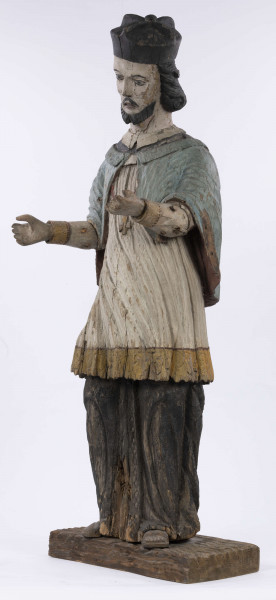 E/8422/ML - Rzeźba drewniana, pełna, polichromowana, przedstawiająca św. Jana Nepomucena. Zakomponowana frontalnie, z rękoma zgiętymi w łokciu i lekko rozłożonymi. Twarz owalna, pomalowana białą farbą. Małą broda i krótkie czarne wąsy. Nos krótki, prosty. Oczy owalne podkreślone czarnym konturem. Brwi łukowate, wąskie, czarne. Włosy czarne, ułożone w pukle. Na głowie czarny biret. Długa czarna sutanna, biała komża ozdobiona u dołu złotą koronką. Na piersiach krzyż, zawieszony na łańcuchu. Na komżę narzucona jasnoniebieska peleryna. Stopy lekko rozstawione. Obuty w sandały o jednym pasku. 

Konserwacja: 1990 r.