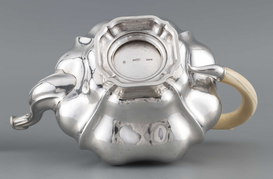 S/Mt/500/ML - Korpus silnie wybrzuszony w części środkowej, puklowany pionowo, profile przechodzą na pokrywke w formie wieczka na zawiasie. Stopa kwadratowa wielolistna, wylew w formie dzióbka, ucho kościane osadzone w dwóch tulejkach,
uchwyt na pokrywce kościany, profilowany. Wnetrze złocone.
Na spodzie stopy sygnatura:
- 