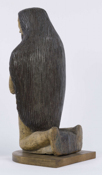 E/6353/ML - Figura drewniana, zakomponowana na postumencie, polichromowana. Postać klęcząca przedstawia św. Onufrego. Twarz płaska, trójkątna, głęboko osadzone oczy, czarne źrenice. Szerokie łuki brwiowe łączą się z wydatnym prostym nosem. Wystające kości jarzmowe. Małe usta otacza bujny zarost: broda i wąsy łączące się z bujnymi włosami, otaczającymi całą postać – na podobieństwo płaszcza. Ręce zgięte w łokciach, uniesione ku górze, łączą się końcami palców w geście modlitwy. W nieproporcjonalnie dużych dłoniach biały różaniec zakończony dużym krzyżem. Nogi masywne z dużymi płaskimi stopami. Prawą dłonią podtrzymuje sękaty kostur. W partii pasa przepasany powrozem z węzłami. 