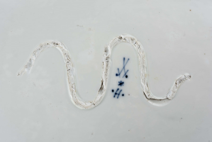 Półmisek owalny, kołnierz gładki o brzegu wykrojonym faliscie. Malowany podszkliwnie kobaltem we wzór tzw. cebulowy, na dnie wieksza kompozycja ze stylizowanych gałązek z kwiatami. Dno wzmocnione od spodu esowatym pasmem z masy porcelanowej.
 