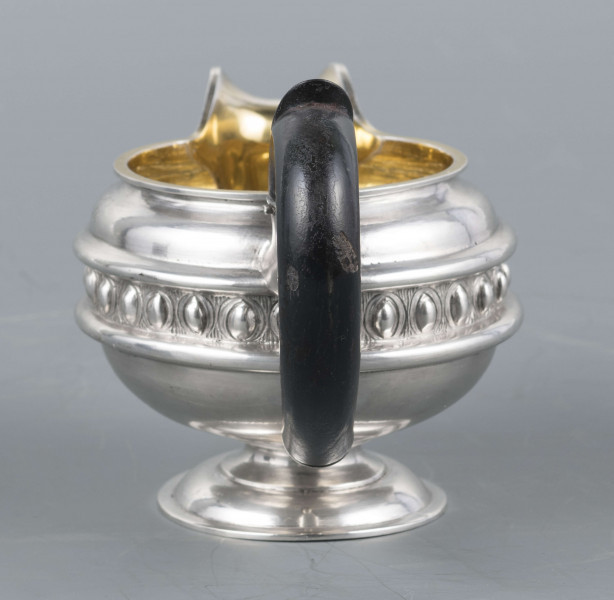 S/Mt/545/ML - Brzusiec w formie spłaszczonej kuli, pośrodku zdobiony repusowanym pasem kimationu obwiedzionego dwoma półwałkami, brzeg górny z okrągłym rantem, wylew wywinięty, zaokrąglony. Wnętrze złocone. Stopa okrągła profilowana, ucho drewniane malowane na czarno, osadzone w dwóch tulejkach . Na brzuscu pod górną krawędzią grawerowany ozdobny monogram 