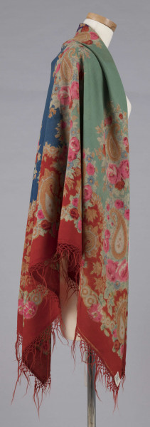 E/7995/ML - Chusta z cienkiej wełny. Powierzchnia podzielona bukietami kwiatów (róże i niezapominajki) na 4 pola w kolorach: czerwonym, zielonym, fioletowym i szafirowym. W każdym narożniku duży bukiet kwiatów oraz tzw. turecki motyw w formie łezki. Bordiura w kolorze czerwonym, na niej wieniec z większych i mniejszych bukietów. Noszona na ramionach. 