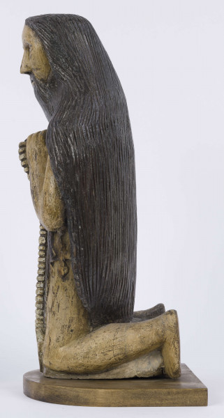 E/6353/ML - Figura drewniana, zakomponowana na postumencie, polichromowana. Postać klęcząca przedstawia św. Onufrego. Twarz płaska, trójkątna, głęboko osadzone oczy, czarne źrenice. Szerokie łuki brwiowe łączą się z wydatnym prostym nosem. Wystające kości jarzmowe. Małe usta otacza bujny zarost: broda i wąsy łączące się z bujnymi włosami, otaczającymi całą postać – na podobieństwo płaszcza. Ręce zgięte w łokciach, uniesione ku górze, łączą się końcami palców w geście modlitwy. W nieproporcjonalnie dużych dłoniach biały różaniec zakończony dużym krzyżem. Nogi masywne z dużymi płaskimi stopami. Prawą dłonią podtrzymuje sękaty kostur. W partii pasa przepasany powrozem z węzłami. 