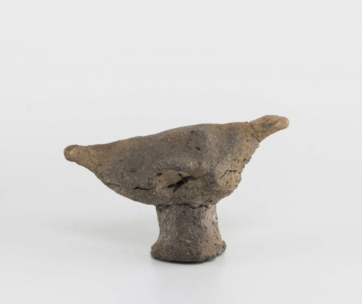 Figurka zoomorficzna w kształcie ptaszka, wykonana schematycznie. Nóżka walcowata. Główka, ogon oraz skrzydełka ledwie zaznaczone. Powierzchnia gładzona niestarannie. Sklejone, uzupełnione gipsem. Surowiec - glina z domieszką drobnoziarnistą. Barwa Szarobrunatna. Wypał dobry.
Wymiary dodatkowe: 1,3 cm (śr. stopki), 2,4 cm (rozstaw skrzydełek)