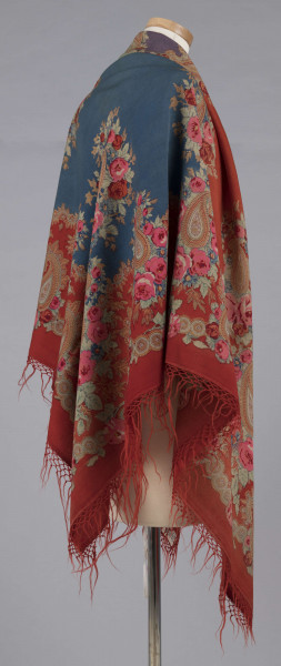 E/7995/ML - Chusta z cienkiej wełny. Powierzchnia podzielona bukietami kwiatów (róże i niezapominajki) na 4 pola w kolorach: czerwonym, zielonym, fioletowym i szafirowym. W każdym narożniku duży bukiet kwiatów oraz tzw. turecki motyw w formie łezki. Bordiura w kolorze czerwonym, na niej wieniec z większych i mniejszych bukietów. Noszona na ramionach. 