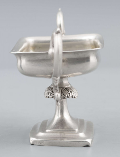 S/Mt/57/ML - Stopa prostokątna, wysklepiona, przechodząca w trzon z owalnym kapturkiem sztancowanym we wzór akantu. Czarka prostokatna o zaokrąglonych narożach i wywinietym brzegu, z dwoma uchami na krótszych bokach. Ucha wolutowe zdobione listkami. 