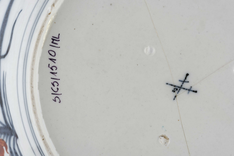 Półmisek okrągły o brzegu falistym. Na kołnierzu szeroka bordiura typu lambrekinowego z dodanymi motywami kwiatowymi, pośrodku dna gałązka kwiatowa, wokół regularnie rozmieszczone mniejsze. Dekoracja dwubarwna: partie kobaltowe malowane pod szkliwem, kwiaty malowane czerwienią naszkliwnie, całość o rysunku podkreślonym złoceniem. Na odwrocie kołnierza malowane gałęzie śliwy i irysów.
 