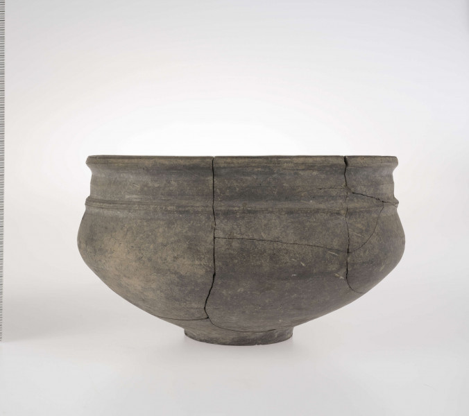 Naczynie o wklęsłym dnie, z dołkiem w centralnej części. Dno wyodrębnione niewysoką stopką. Brzusiec łagodnie profilowany. Szyjka podkreślona plstyczną listwą, w części środkowej nieco wypukła. Krawędź wylewu delikatnie wywinięta na zewnątrz. 