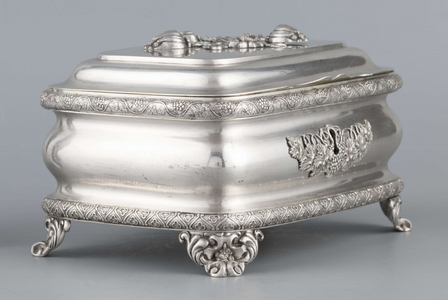 S/Mt/469/ML - Cukiernica prostokątna o zaokrągłonych narożach, profilowana, na czterech akantowych nóżkach. Brzeg dolny i górny obwiedzione półwałkiem zmoletowanej taśmy: u góry z wzorem winorośli, na dole - trójliścia.Brzeg wieczka fasetowany, z przodu lekko wywinięty tworzy uchwyt. Na wieczku nałożona półplastyczna plakieta w postaci  asymetrycznej gałązki kwiatowej. Szyld zamka stanowi sztancowana plakieta z motywem winorośli. Wnętrze złocone.
Na dnie sygnatura wypukła we wklęsłych ramkach:
- J.Suchocki
- w Lublinie
i punca z oznaczeniem próby 