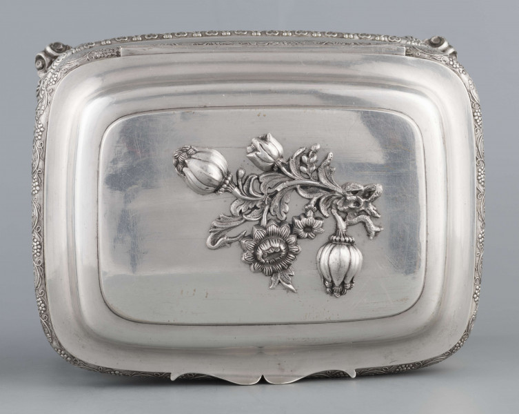 S/Mt/469/ML - Cukiernica prostokątna o zaokrągłonych narożach, profilowana, na czterech akantowych nóżkach. Brzeg dolny i górny obwiedzione półwałkiem zmoletowanej taśmy: u góry z wzorem winorośli, na dole - trójliścia.Brzeg wieczka fasetowany, z przodu lekko wywinięty tworzy uchwyt. Na wieczku nałożona półplastyczna plakieta w postaci  asymetrycznej gałązki kwiatowej. Szyld zamka stanowi sztancowana plakieta z motywem winorośli. Wnętrze złocone.
Na dnie sygnatura wypukła we wklęsłych ramkach:
- J.Suchocki
- w Lublinie
i punca z oznaczeniem próby 