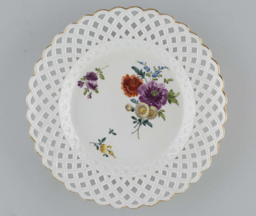 Talerz płytki z kołnierzem ażurowym o wzorze ukośnej plecionki, która przechodzi na powierzchnię fasety. W lustrze malowana dekoracja wielobarwna w układzie asymetrycznym: bukiet kwiatów z purpurowym makiem, dwie kwitnące gałązki i pojedynczy listek.
 