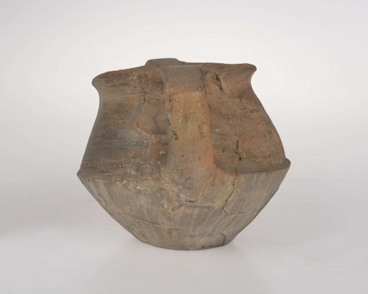 Naczynie wazowate, dwustożkowe z dwoma taśmowatymi uchami. Nad załomem brzuśca zdobienie w postaci linii rytych wypełnionych ukośnym kreskowaniem. Powierzchnia brunatna. Typ III/3 wg T. Liany.