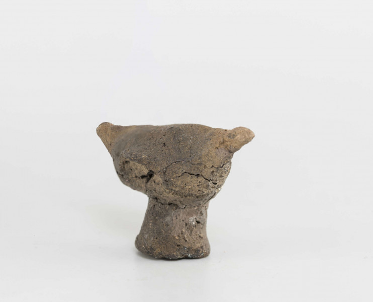 Figurka zoomorficzna w kształcie ptaszka, wykonana schematycznie. Nóżka walcowata. Główka, ogon oraz skrzydełka ledwie zaznaczone. Powierzchnia gładzona niestarannie. Sklejone, uzupełnione gipsem. Surowiec - glina z domieszką drobnoziarnistą. Barwa Szarobrunatna. Wypał dobry.
Wymiary dodatkowe: 1,3 cm (śr. stopki), 2,4 cm (rozstaw skrzydełek)