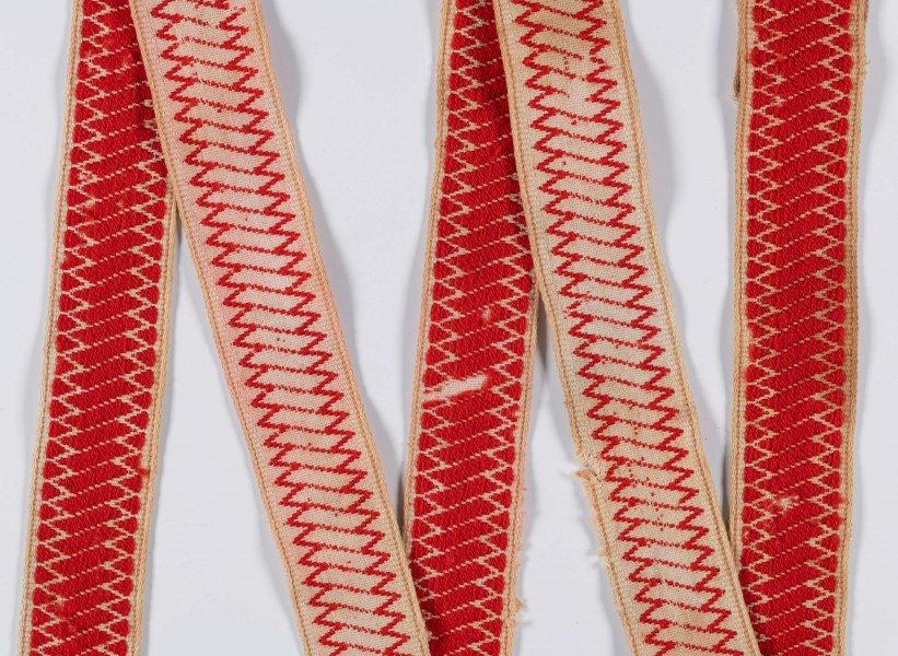 E/12133/ML - Kolorowa krajka. Na bawełnianym płótnie tkanym splotem prostym znajduje się przetykany ornament geometryczny koloru czerwonego.

