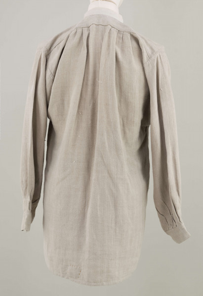 E/9858/ML - Koszula męska z lnianego samodziałowego płótna tkanego splotem prostym, szyta na maszynie. Krój z karczkiem. Wycięcie koło szyi wykończone stójką z białego płótna zapinana na jeden guziczek. Rozcięcie na przodzie o dł. 26 cm zapinane na dwa guziczki, wykończone fałdem o szer. 4,5 cm. Gors naszyty jest cienkim białym płótnem. Rękawy długie, krojone, razem z włokami dołem wzbogacone ośmioma zakładkami ujęte w mankiet o dł. 24 cm szer. 4 cm zapinany na guziczek.