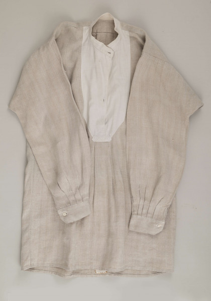 E/9858/ML - Koszula męska z lnianego samodziałowego płótna tkanego splotem prostym, szyta na maszynie. Krój z karczkiem. Wycięcie koło szyi wykończone stójką z białego płótna zapinana na jeden guziczek. Rozcięcie na przodzie o dł. 26 cm zapinane na dwa guziczki, wykończone fałdem o szer. 4,5 cm. Gors naszyty jest cienkim białym płótnem. Rękawy długie, krojone, razem z włokami dołem wzbogacone ośmioma zakładkami ujęte w mankiet o dł. 24 cm szer. 4 cm zapinany na guziczek.