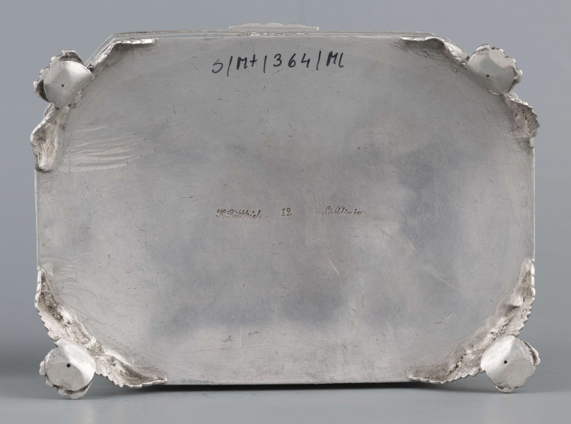 S/Mt/364/ML - Cukiernica skrzynkowa prostokątna ze ściętymi narożami, na czterech nóżkach w formie uskrzydlonych lwich łap, z wieczkiem o wklęsło profilowanym brzegu. Górny i dolny brzeg obiega  moletowana taśma z motywem neogotyckich trójliści, szyld zamka ma formę różanego wieńca pod skrzydatą główką..W ścianki i wieczko wmontowanych jest 15 monet srebrnych:
1 ort Zygmunta III
1 talar pruski, 1818 r.
1 pięciofrankówka, 1811 r.
1 moneta austriacka, 1797 r.
1 moneta saska, 
2 monety polskie St.Augusta Poniatowskiego
1 dwózłotówka Królestwa Polskiego, 1825 r.
1 pięciozłotówka, 1831 r.
6 złotówek, 1831 r.
Na dnie sygnatura wklęsła kursywą:
- K. Rotkiel w Lublinie
i punca z oznaczeniem próby 