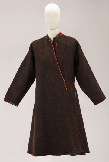 Sukmana męska, odświętna, szyta ręcznie z samodziałowego, folowanego sukna w kolorze ciemnobrązowym. Uszyta z 7 części: rękawy z jednego kawałka, zwężone ku dołowi, przody, plecy i dwa kliny uzupełniające fałdowanie poniżej talii z tyłu. Przody gładkie rozszerzone lekko ku dołowi, ozdobione przy zapięciu pomarańczowym sznureczkiem, który ozdabia również wycięcie wokół szyi. Tył sukmany, poniżej talii, fałdowany – po bokach symetrycznie ułożone po 3 fałdki o szer. 4 cm. W bokach, poniżej talii, rozcięcia tworzące ślepe kieszenie. Przy kieszeniach i wokół fałdowania obszycia proste z pomarańczowego sznurka.