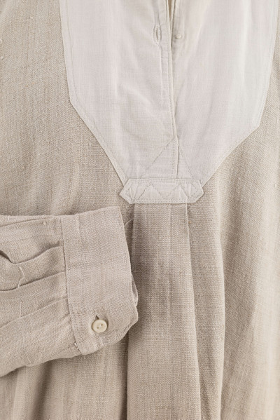 E/9858/ML - Koszula męska z lnianego samodziałowego płótna tkanego splotem prostym, szyta na maszynie. Krój z karczkiem. Wycięcie koło szyi wykończone stójką z białego płótna zapinana na jeden guziczek. Rozcięcie na przodzie o dł. 26 cm zapinane na dwa guziczki, wykończone fałdem o szer. 4,5 cm. Gors naszyty jest cienkim białym płótnem. Rękawy długie, krojone, razem z włokami dołem wzbogacone ośmioma zakładkami ujęte w mankiet o dł. 24 cm szer. 4 cm zapinany na guziczek.