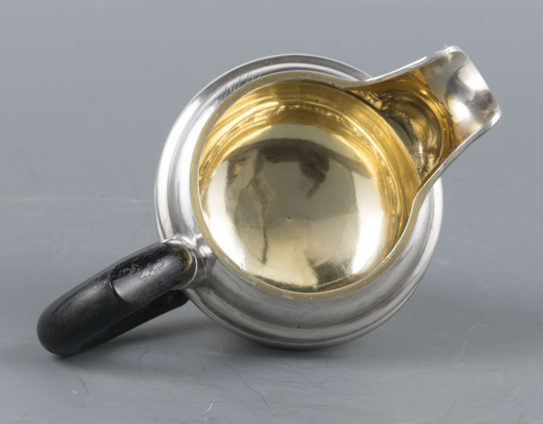 S/Mt/545/ML - Brzusiec w formie spłaszczonej kuli, pośrodku zdobiony repusowanym pasem kimationu obwiedzionego dwoma półwałkami, brzeg górny z okrągłym rantem, wylew wywinięty, zaokrąglony. Wnętrze złocone. Stopa okrągła profilowana, ucho drewniane malowane na czarno, osadzone w dwóch tulejkach . Na brzuscu pod górną krawędzią grawerowany ozdobny monogram 