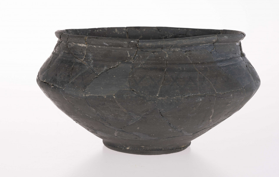 Naczynie wazowate - dwustożkowate; dno lekko wklęsłe z dołeczkiem w środku, wyraźnie wyodrębnione niewielką stopką; brzusiec dwustożkowaty, ostro profilowany; miejsce przejścia brzuśca w szyję zaznaczone wypukłą dookolna listwą; szyja niska, cylindryczna; wylew zaokrąglony, wywiniety na zewnatrz; górna część brzuśca zdobiona dookolnym rzędem narysowanych 