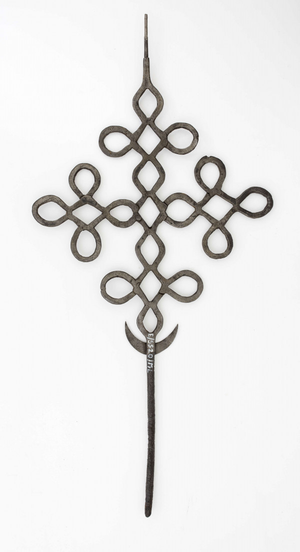 Krzyż o ramionach wykonanych z płaskich prętów żelaznych, powyginanych w ten sposób, że tworzą małe krzyżyki. W dolnej części krzyża przynitowany półksiężyc. Dolny koniec środkowego ramienia w postaci obłego pręta.