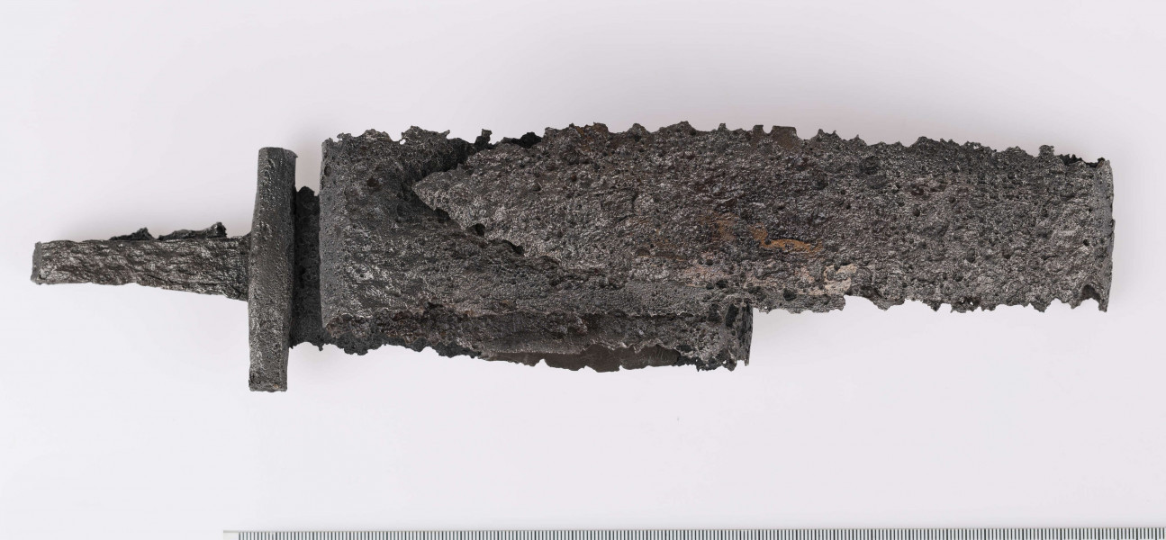 Miecz żelazny, obosieczny, bez strużyn. U podstawy trzpienia znajduje się krótki, prosty w przekroju czworoboczny jelec. Kolec prosty na końcu rozklepany. Miecz rytualnie zgięty.