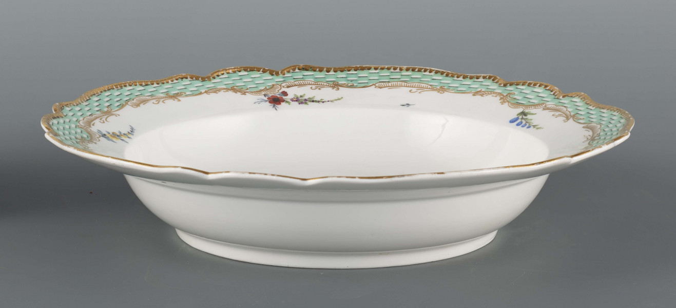 S/CS/1580/ML - Talerz głęboki o falistym wykroju brzegu. Na dnie malowana barwna miniatura przedstawiajaca scenkę w pejzażu: chłopiec wpadł do strumienia i trzyma się gałązki wierzby rosnacej na brzegu, obok stoi nauczyciel z rózgą w ręce. Na kołnierzu malowana mozaika w kolorze zieleni miedziowej, obramowana od środka złotymi rocaille'ami z piecioma rzuconymi gałązkami. 
Na spodzie napis wykonany naszkliwnie purpurą: 