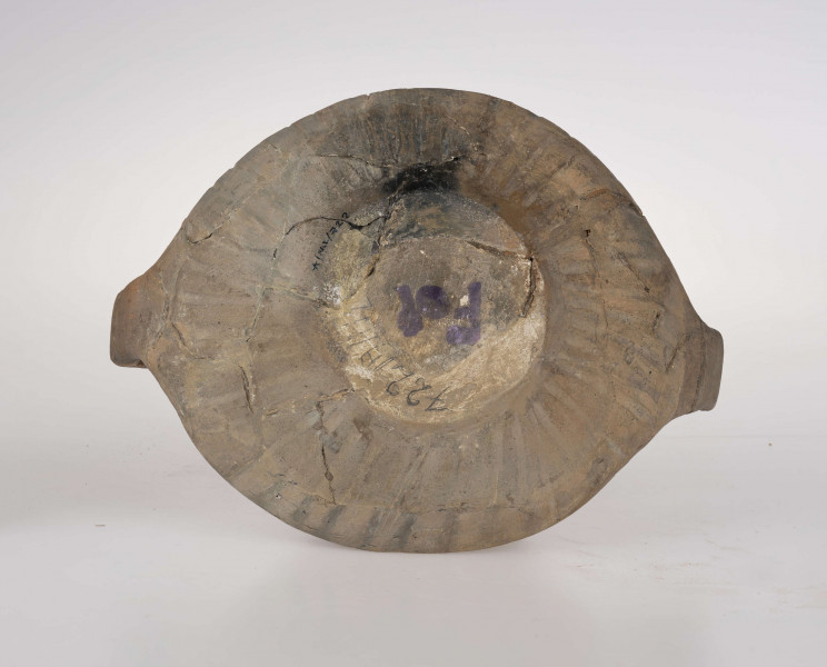 Naczynie wazowate, dwustożkowe z dwoma taśmowatymi uchami. Nad załomem brzuśca zdobienie w postaci linii rytych wypełnionych ukośnym kreskowaniem. Powierzchnia brunatna. Typ III/3 wg T. Liany.