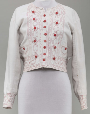 Kaftan kobiecy wykonany z tkaniny bawełnianej (piki), koloru białego. Ozdobiony stebnówką koloru czerwonego i zielonego oraz czerwonymi guzikami. Na lnianej podszewce.