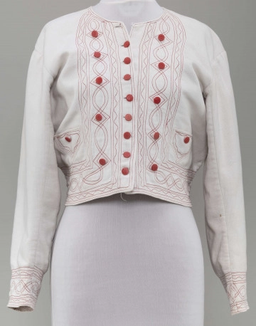 Kaftan kobiecy wykonany z tkaniny bawełnianej (piki), koloru białego. Ozdobiony stebnówką koloru czerwonego i zielonego oraz czerwonymi guzikami. Na lnianej podszewce.