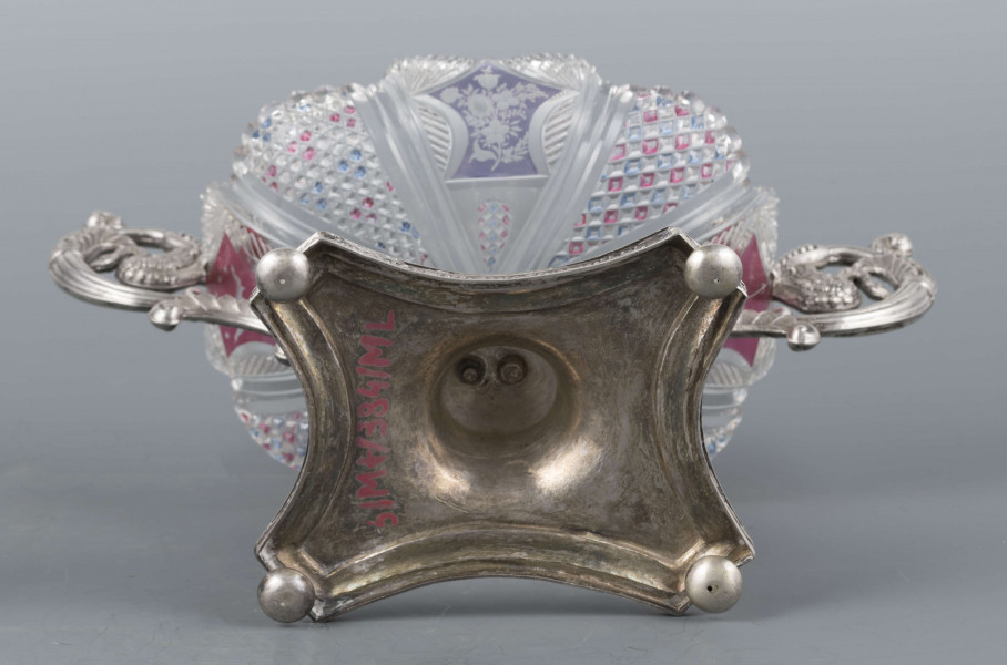 S/Mt/384/ML - Czara ze szkła bezbarwnego, miejscami barwionego powierzchniowo, płytka, owalna, profilowana, z dekoracją szlifowaną (wachlarzyki i szlif brylantowy) i trawioną (wzór kwiatowy) - utrzymana w stylu biedermeier. Umieszczona na figurce delfina z podstawą czworoboczną o wklęsłych bokach i ściętych narożach, z nóżkami w kształcie spłaszczonych kulek. Po bokach czary ucha w formie wolut z liśćmi akantu i motywem łabędzi. Brzeg podstawy obiega pas wici różanej.
Na brzegu podstawy sygnatura wklęsła kursywą: 
-  